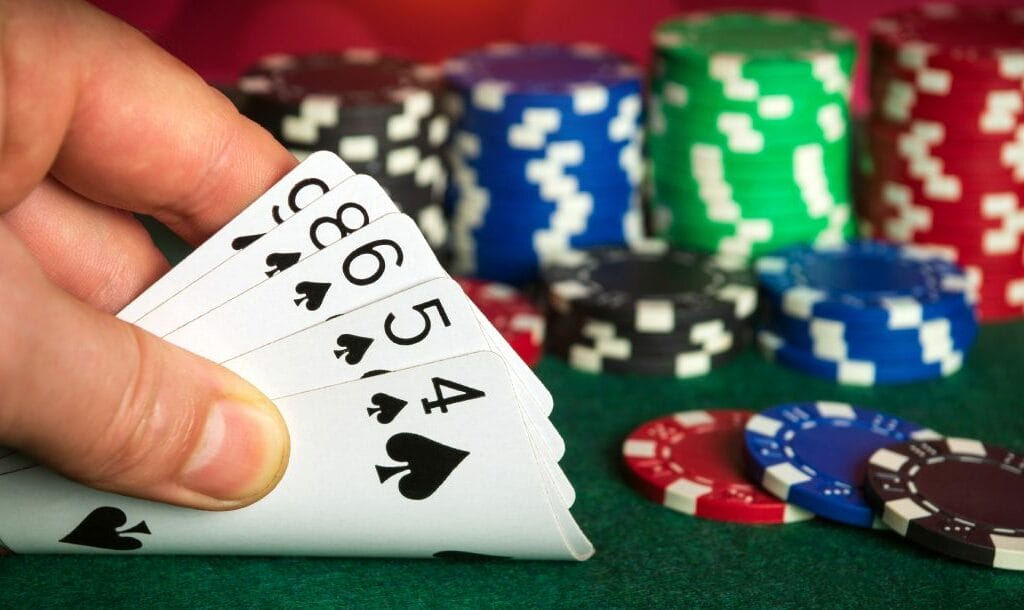 A hand revealing playing cards with poker chips on the table.