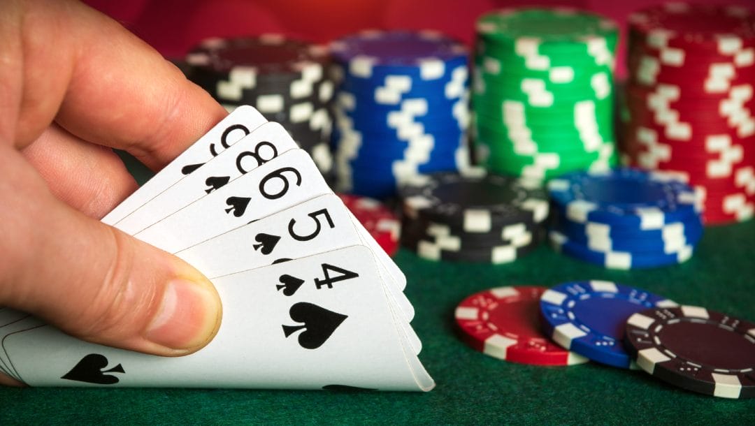 A hand revealing playing cards with poker chips on the table.