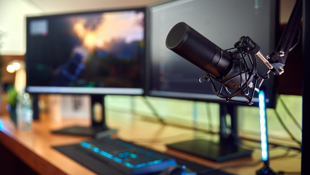 A home streaming setup with a microphone on a boom, dual monitors, an RGB keyboard and mouse.