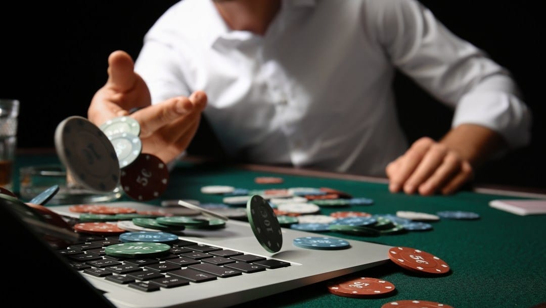 A poker player tosses poker chips toward a laptop computer.