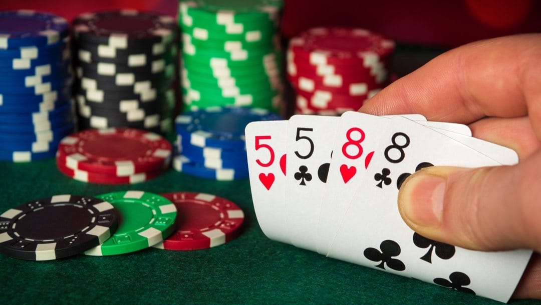 A poker player checks their hand and sees a pair of fives and a pair of eights.