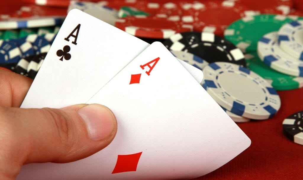 A poker player looks at their hole cards and sees two aces. There are poker chips scattered on the table behind them.