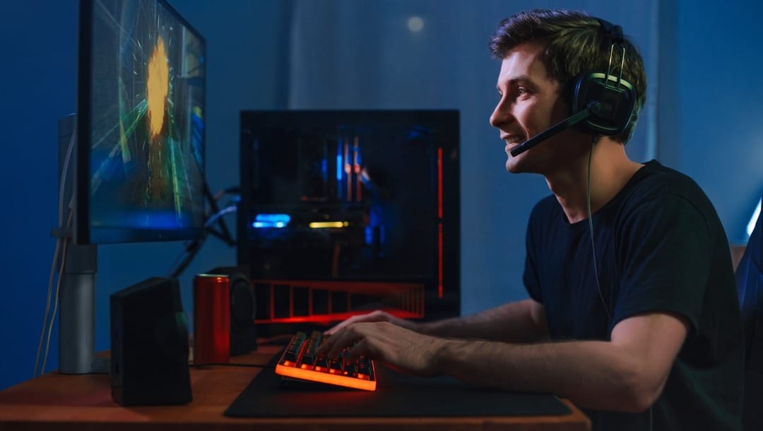 A young man wearing a headset playing games on a computer with RGB lighting.