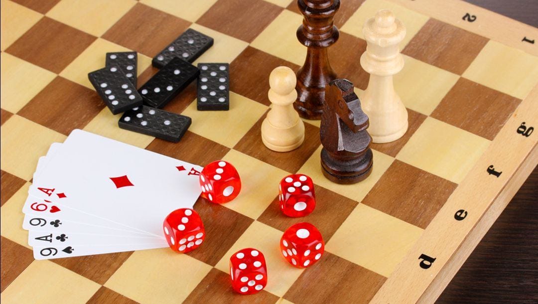 Dice, playing cards, domino pieces and chess pieces on a chess board.