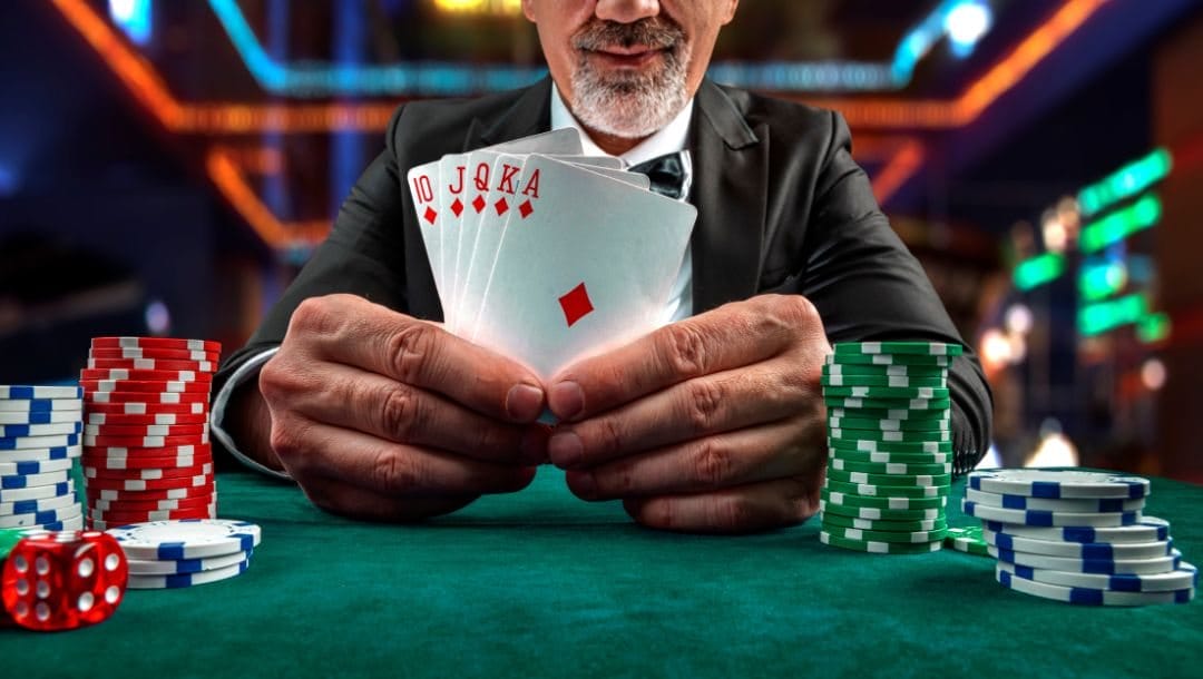 A man showing a royal flush of diamonds on a poker table in between stacks of poker chips