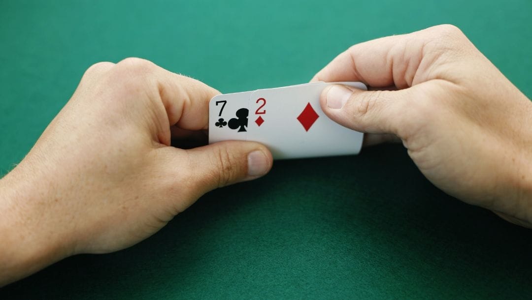 Man holding his starting hand of a club seven and diamond two