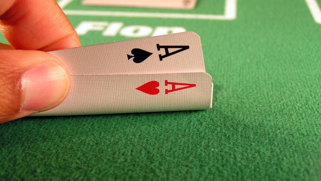 A man’s hand lifting up his starting hand of a pocket pair of aces