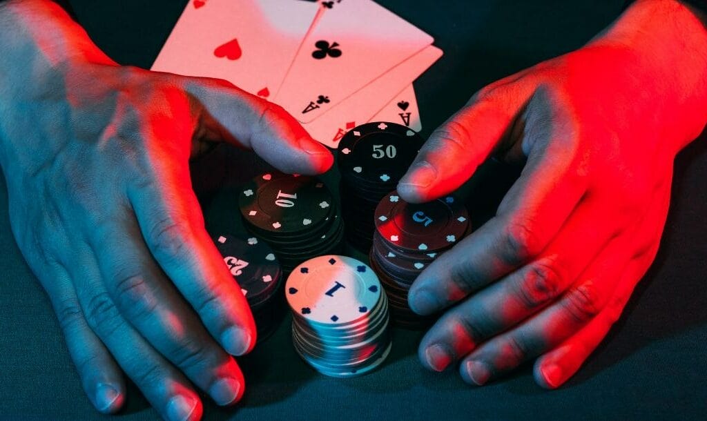 A man’s hand claiming poker chips with a winning hand of four aces