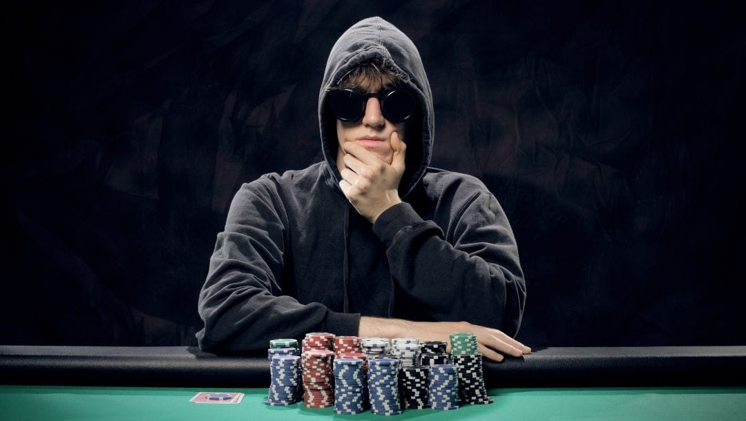 Young man sitting at a poker table wearing sunglasses with stacks of poker chips in front of him