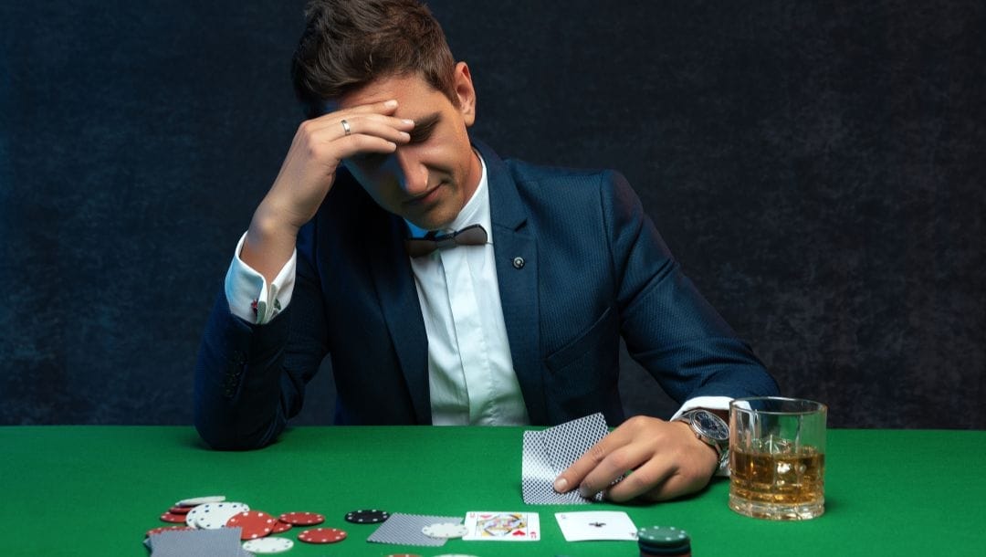 Man sitting at a poker table looking at his hand with a stressed facial expression