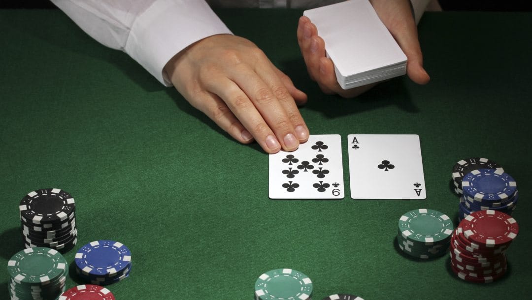 Poker dealer holding a pack of white cards, with two cards dealt on the table and poker chips stacked in front of them.