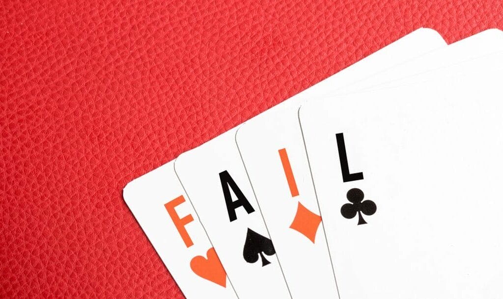 Four playing cards with the ranks replaced to spell the word “FAIL” out, lying on a red leather table.