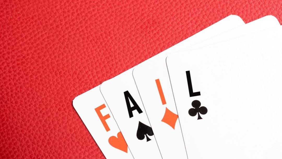 Four playing cards with the ranks replaced to spell the word “FAIL” out, lying on a red leather table.