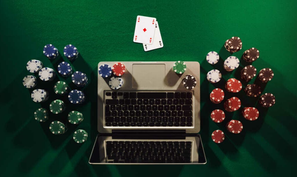 Aerial view of a laptop with poker chips and two cards on a table