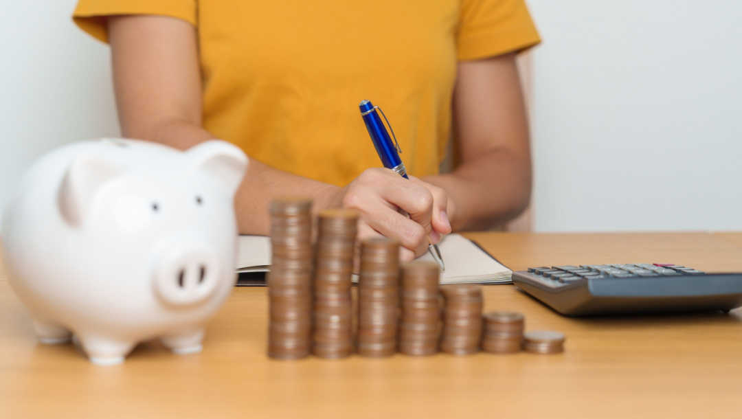A woman working out finances with a piggy bank, coins and a calculator on the desk
