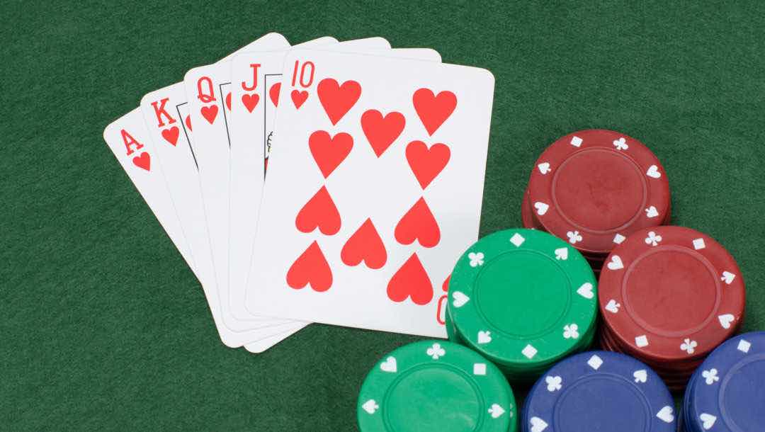 A royal flush next to stacks of poker chips on a green poker table.