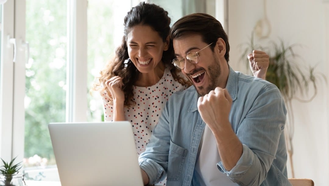 Two people celebrate together while looking at a laptop screen.