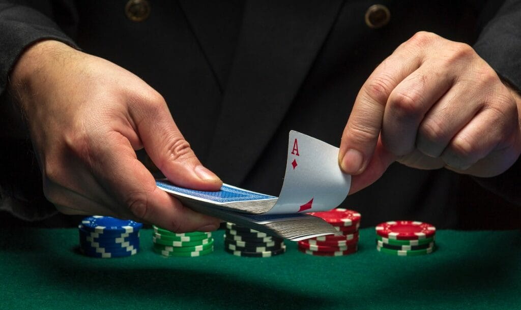 A croupier pulls an ace from a deck of cards over a green felt table with poker chips.