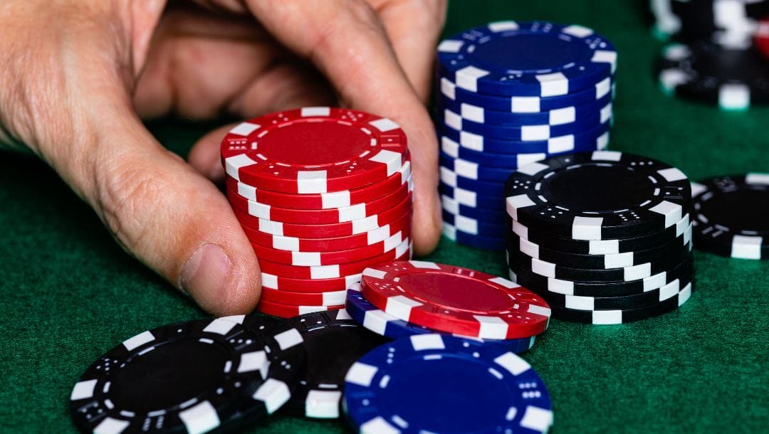 a man picking up a stack of poker chips on a green felt poker table