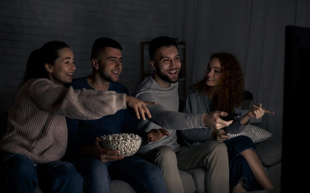 A group of friends sitting on a couch watching a movie.