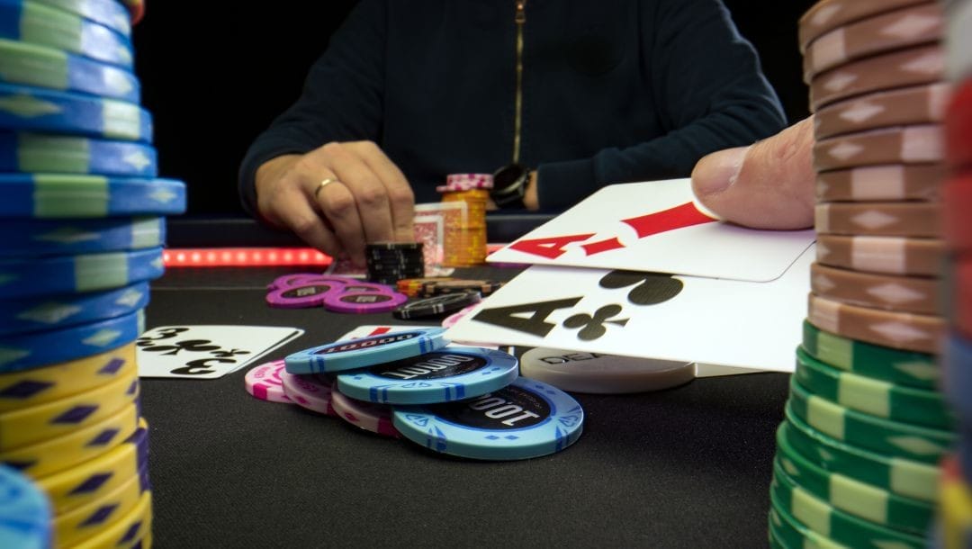the view of a poker game through two stacks of poker chips, a pair of aces held towards a pile of poker chips with a man sitting opposite at the table