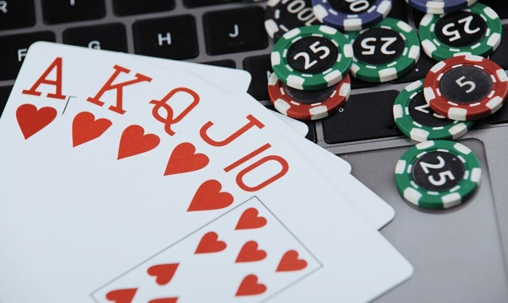 A royal flush on a laptop keyboard next to scattered poker chips.