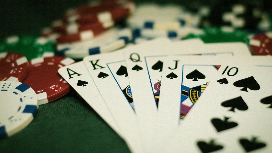 five playing cards ten, jack, queen, king, ace of spades, fanned out on poker chips on a green felt poker table