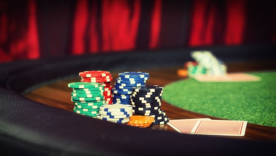 Close up of the rim of a green felt poker table, stacks of poker chips and a pair of playing cards laying face down on the wooden outer edge of the table
