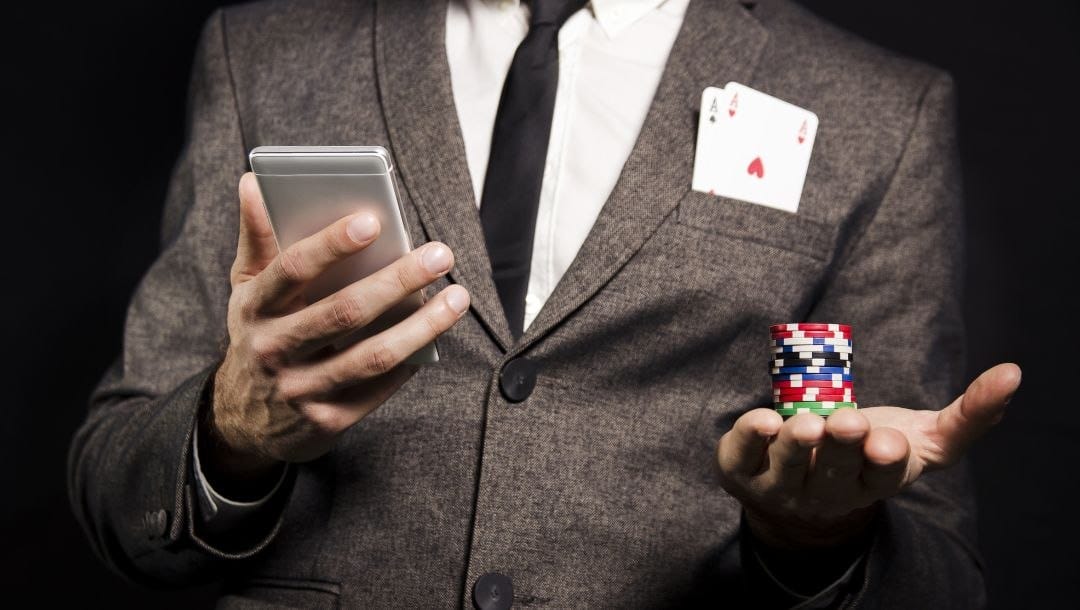 Body image, Man in a suit holding a cellphone in his right hand and a stack of poker chips in his left hand, pocket aces are sticking out of his pocket square