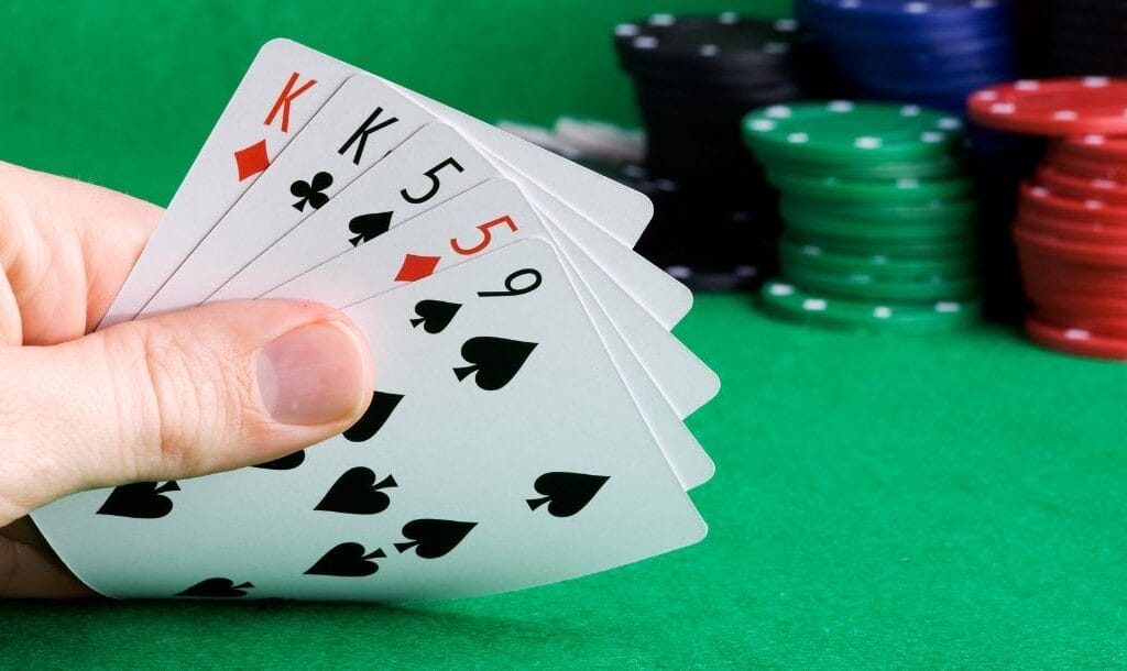 a hand of five playing cards on a green felt poker table with poker chips stacked behind