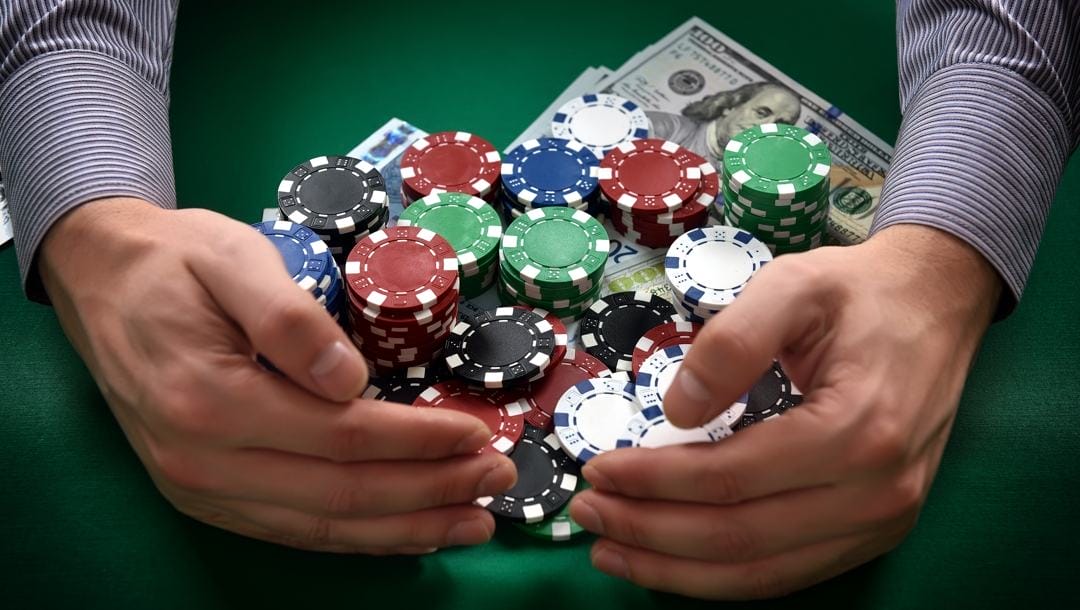 A poker player pulls a pile of poker chips and cash toward themselves.
