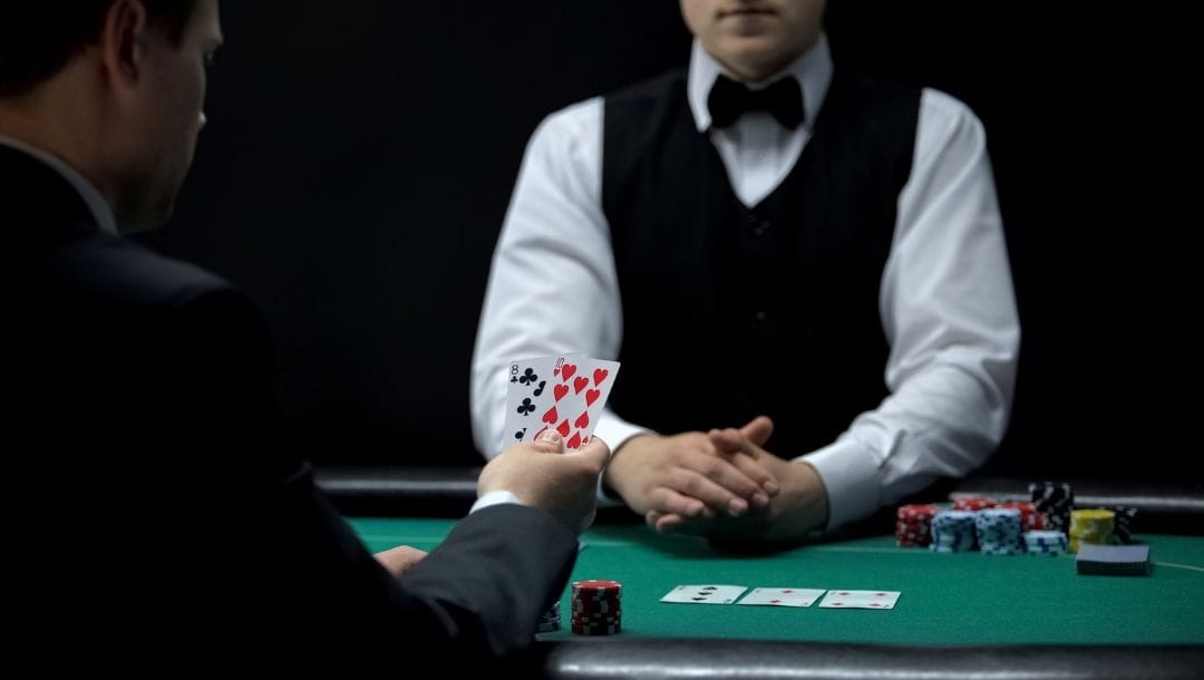 A man sitting at a poker table opposite the croupier checking his hole cards during a game of poker