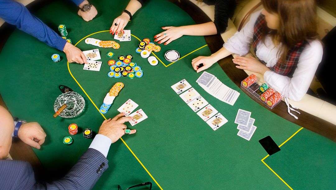 Top view of people playing poker around a green felt poker table, players arms are reaching in to show their cards