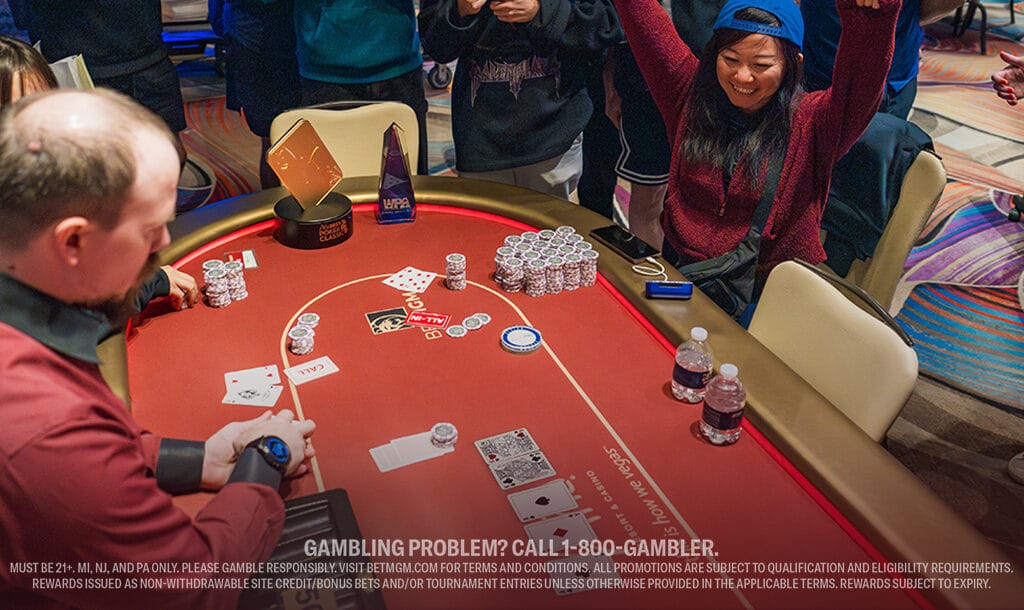 A player cheers triumphantly with raised arms beside a poker table, surrounded by chips and cards. An engaged crowd observes, creating an excited atmosphere.