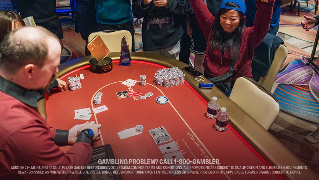 A player cheers triumphantly with raised arms beside a poker table, surrounded by chips and cards. An engaged crowd observes, creating an excited atmosphere.