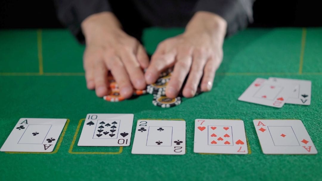 a man’s hands are covering poker chips on a green felt poker surface, in front of him are playing cards post-flop during a game of poker