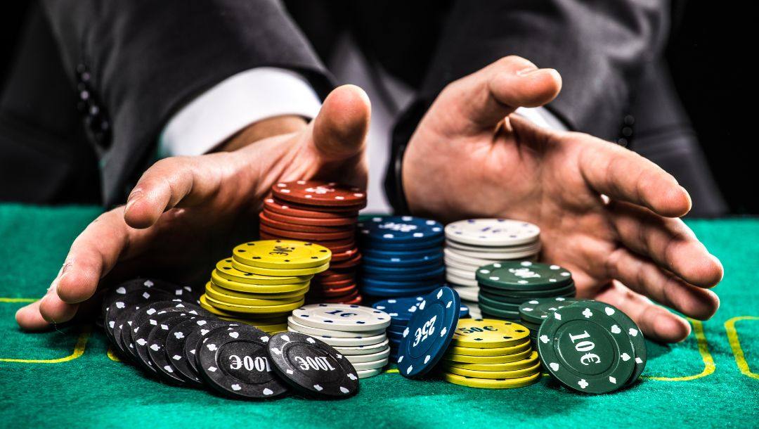 a man’s hands pushing stacks of poker chips forward on a green felt poker table