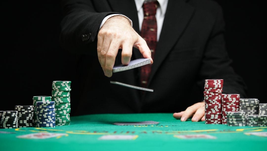 a dealer shuffling playing cards on a green felt poker table with poker chips stacked on each side