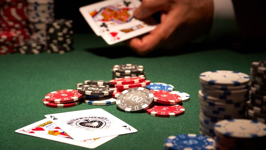 two sets of poker hands, a pair of queens and a king ace, and a pot of poker chips in the middle on the green felt poker table