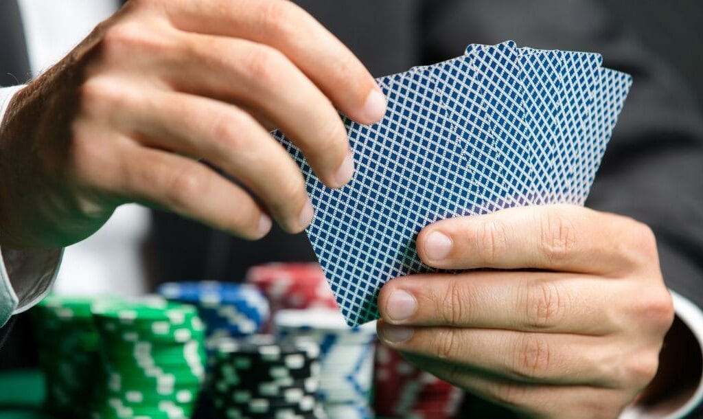 a close up of a man holding playing cards in his hands above a green felt poker table that has poker chips stacked on it