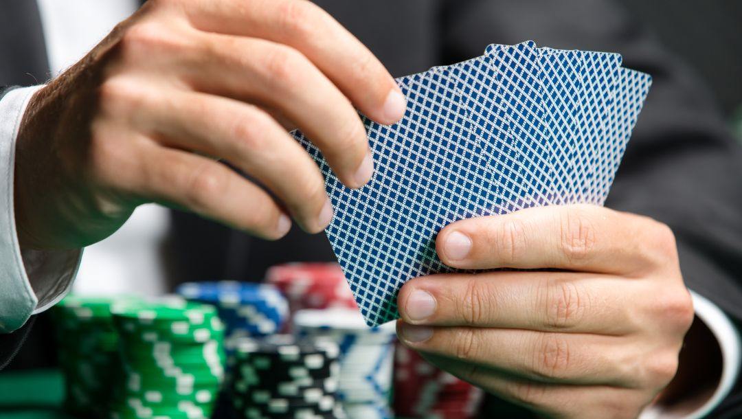 a close up of a man holding playing cards in his hands above a green felt poker table that has poker chips stacked on it