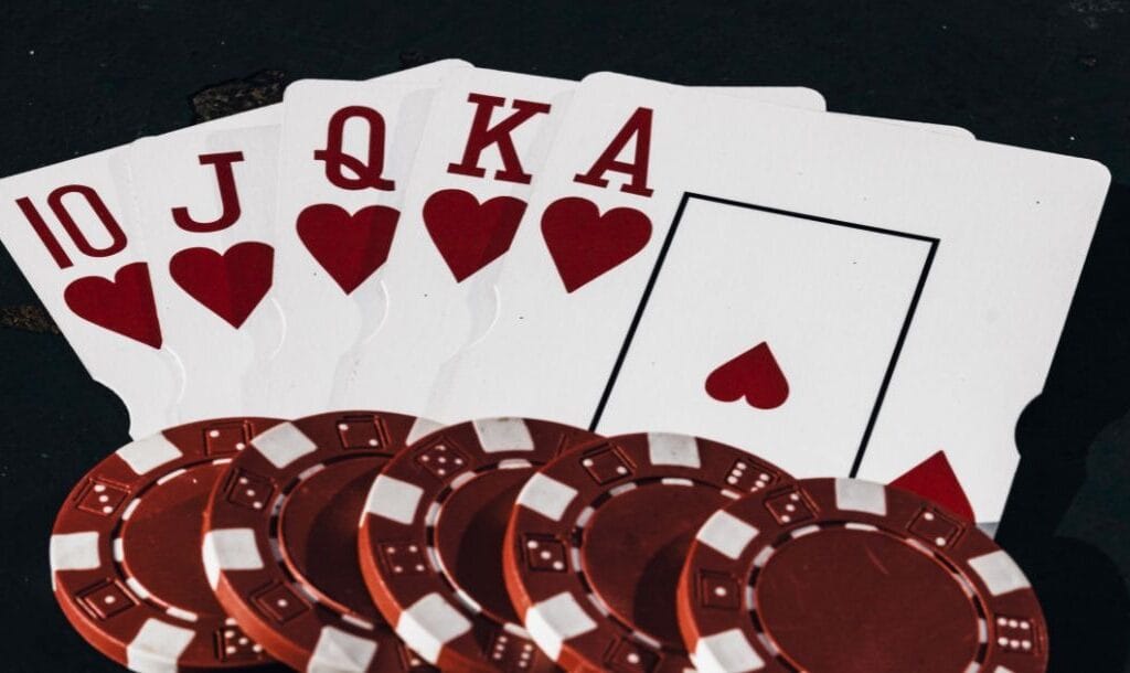 a royal flush of hearts playing cards with five red poker chips on the bottom of them on a dark surface