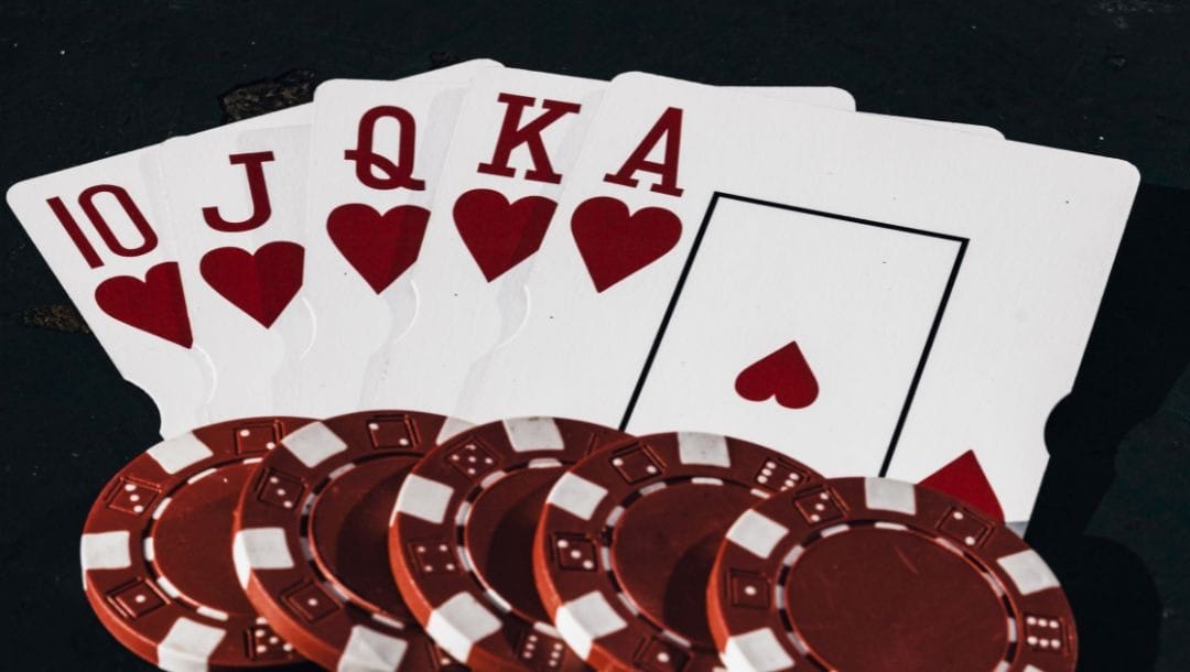a royal flush of hearts playing cards with five red poker chips on the bottom of them on a dark surface