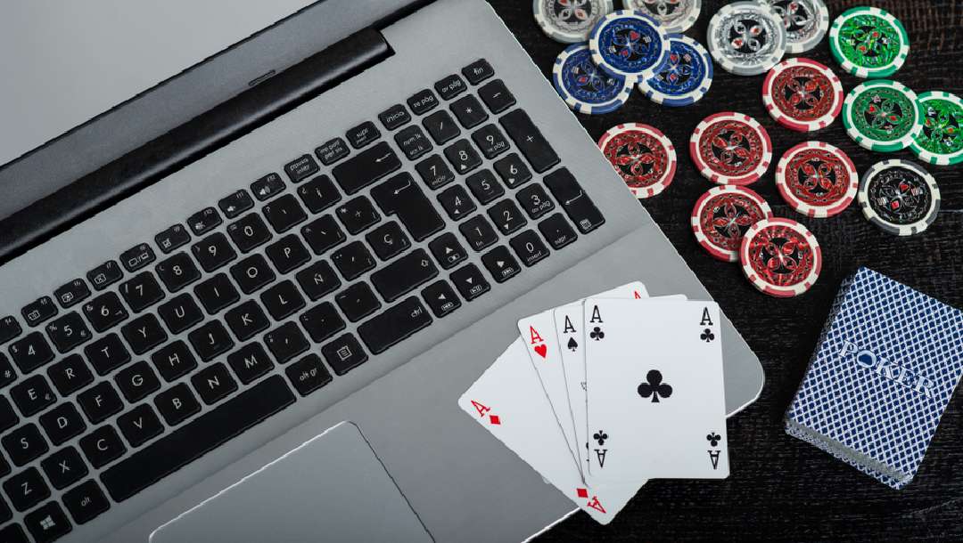 A laptop with poker chips and cards next to it