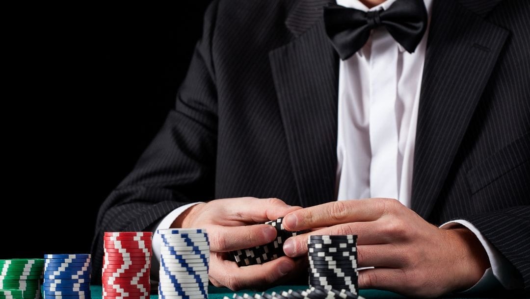 a man wearing a suit with a bowtie is sitting at a poker table with poker chips stacked in front of him