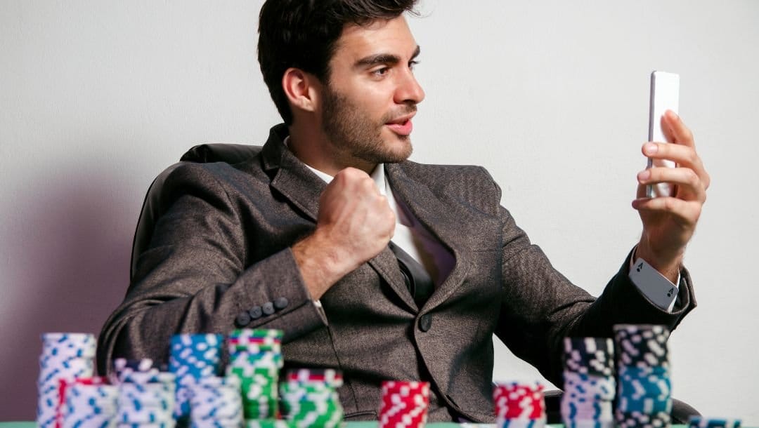 a man is celebrating with a fist and holding a cellphone in his other hand while sitting at a table stacked with poker chips on it