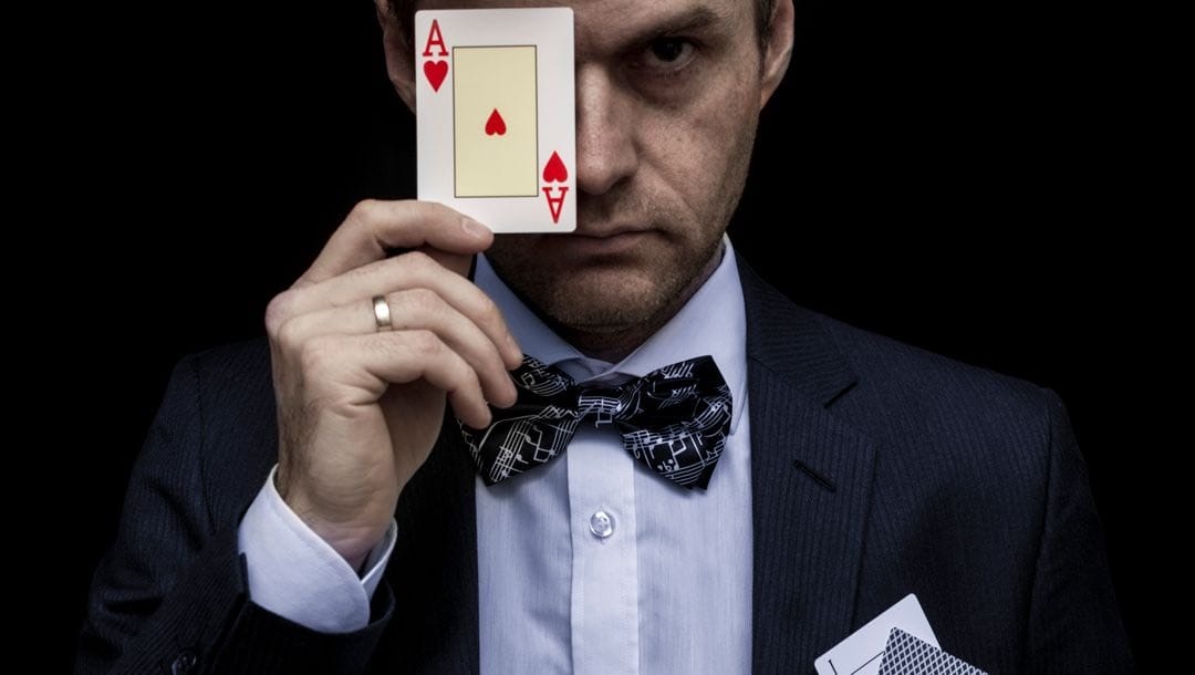 A man in a tuxedo holding an ace of hearts up against his face.