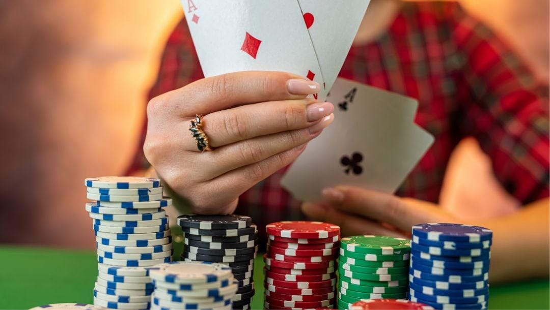 poker chips stacked up on a green felt poker table, a lady wearing a ring is holding up four ace playing cards in the background