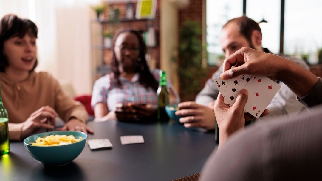 friends gathered around an at-home dining table while playing poker, on the table there are drinks and snacks