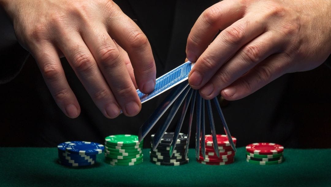 a man shuffling cards above a green felt poker table with five stacks of poker chips on it